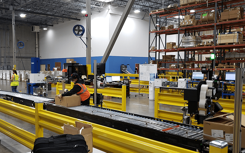 Workers in a warehouse remove packages from a conveyor belt. Four strategies to reduce warehouse labor costs.